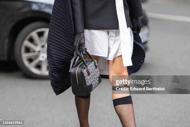 Miss Fame wears a white long shirt dress, a black blazer jacket with a black ribbed embroidered cape / cloak in the back from Loewe, black gloves, a...