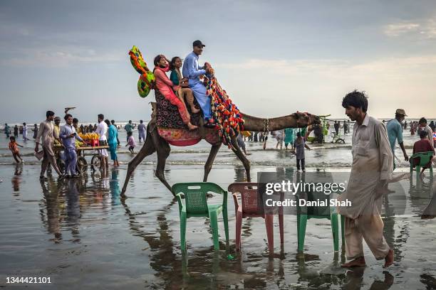 People ride a camel along the beach as dusk approaches at Clifton Beach on September 19, 2021 in Karachi, Pakistan. Clifton Beach, also known by many...