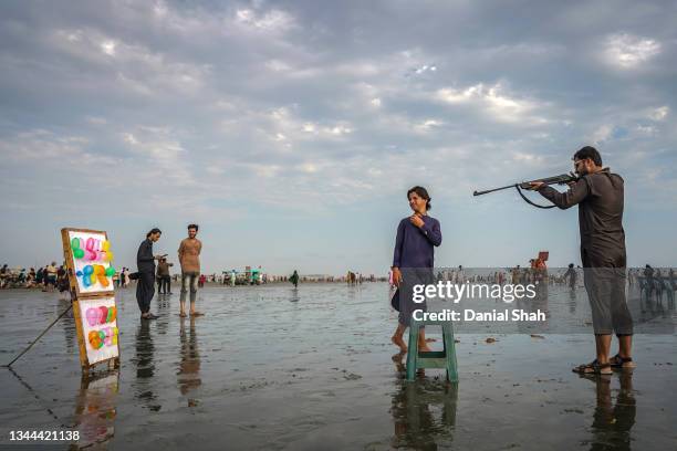 Man uses an air rifle to shoot balloons at an improvised amusement stall as dusk approaches at Clifton Beach on September 19, 2021 in Karachi,...