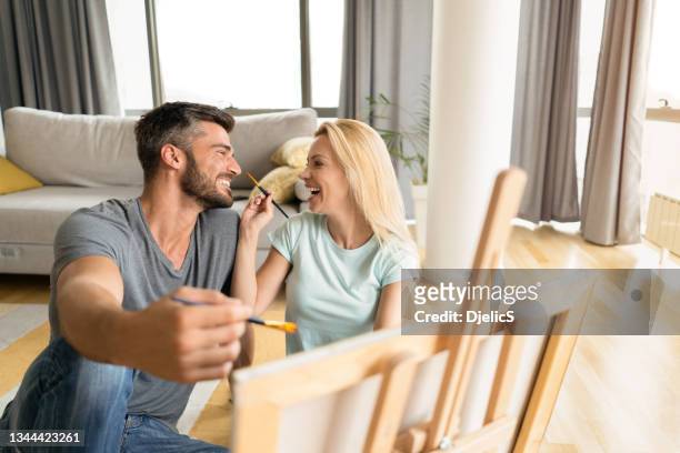 young couple painting a picture together in the living room. - house for an art lover stock pictures, royalty-free photos & images