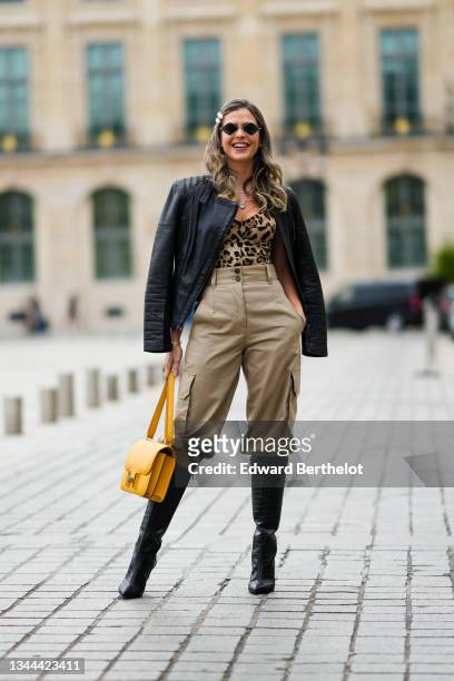 Passerby wears sunglasses, white hair-clips, silver earrings, silver chain necklaces, a black shiny leather biker jacket, a brown / beige / black...