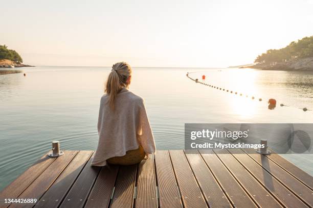 junge frau, die sich bei sonnenaufgang am pier entspannt und den meerblick genießt - bootssteg stock-fotos und bilder