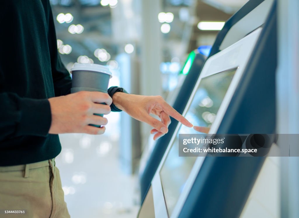 Young Asian man travelling by plane and doing self check in at the airport using a machine