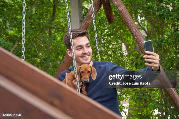 guy posing with dachshund for a picture on the mobile phone outdoors.pet and people concept - park man made space stock pictures, royalty-free photos & images