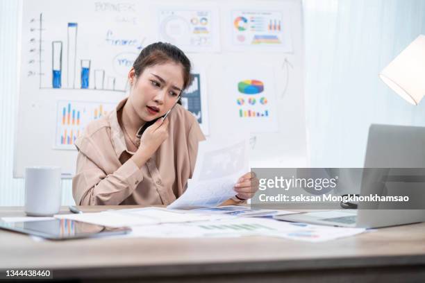 stressed businesswoman taking a phone call at her desk - asking money stock pictures, royalty-free photos & images