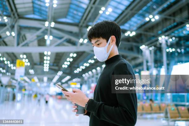 young asian man checking departure board with smart phone at the airport - máscara de mergulho imagens e fotografias de stock