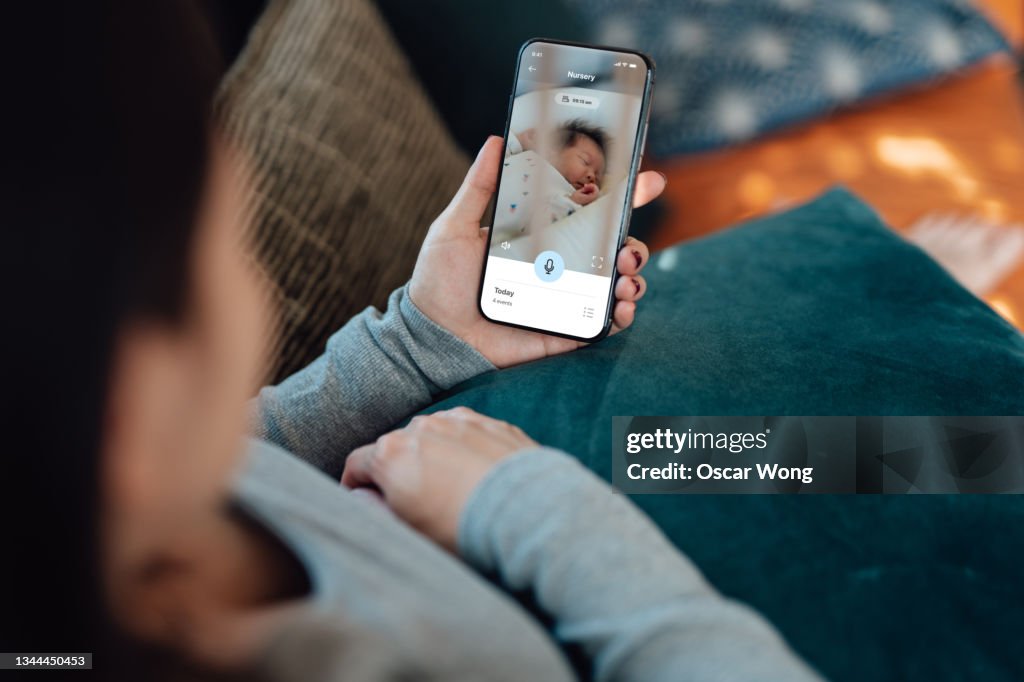 Young mother using baby monitor app on her smart phone while sitting in the living room