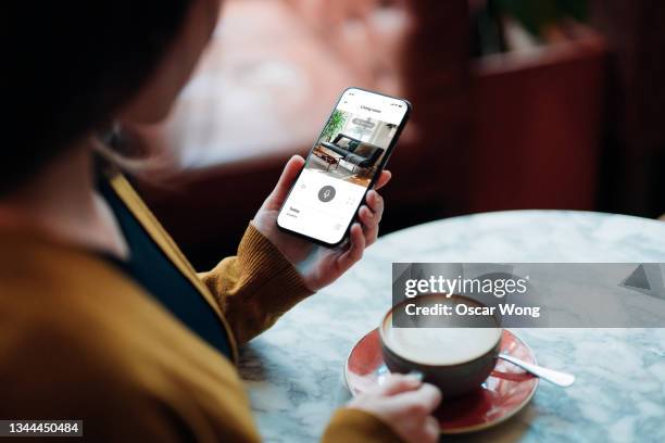 young woman monitoring her home from smart phone while enjoying coffee at cafe - bewakingscamera stockfoto's en -beelden