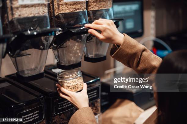 close-up of woman dispensing oats into jar at whole food refill store - filling jar stock pictures, royalty-free photos & images