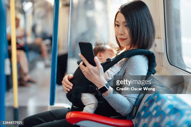 young mother using smart phone while travelling with her newborn baby on subway - safe kids day stock pictures, royalty-free photos & images