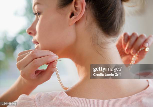 woman putting on pearl necklace - jewelry necklace stockfoto's en -beelden