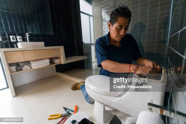 latin american plumber fixing a toilet in the bathroom - plumber stockfoto's en -beelden