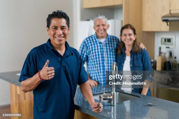 happy plumber with thumbs up after repairing a kitchen for a couple at their home - plumber man stockfoto's en -beelden