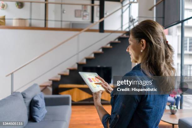 woman controlling the ambiance of her house using a home automation system - smart house stock pictures, royalty-free photos & images