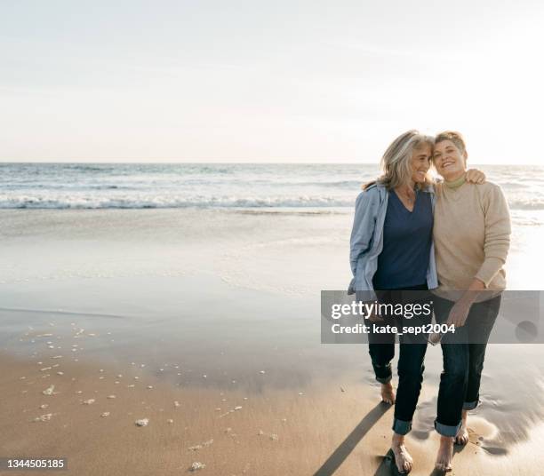 two beautiful senior woman on their barefoot walk - lesbisch stockfoto's en -beelden