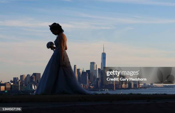 Girl wears her quinceanera dress as she waits to have her picture taken in front of the skyline of lower Manhattan in New York City as the sun sets...