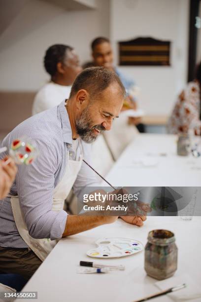 smiling mature man painting on glass in an art and craft class - art class stockfoto's en -beelden