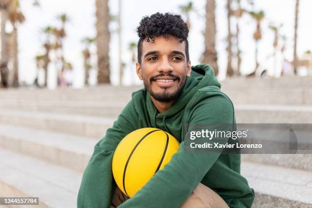 young basketball player sitting outdoors - young man holding basketball stockfoto's en -beelden