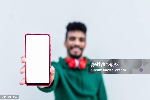 happy hispanic man showing mobile phone with white screen - presenteren stockfoto's en -beelden