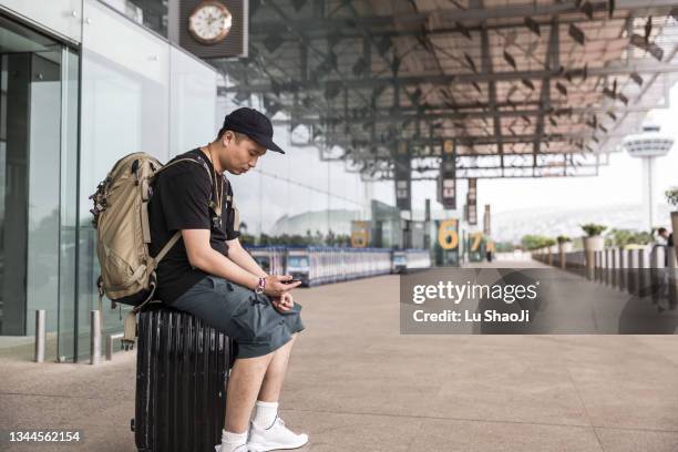 tourists sit on the suitcases outside the airport terminal. - carrying sign ストックフォトと画像