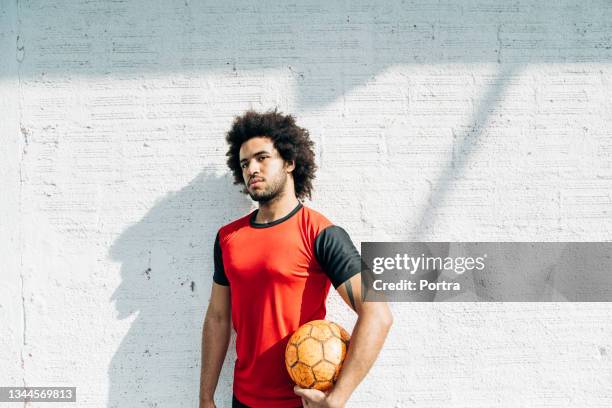 young male soccer player standing by a while wall - red sports jersey stock pictures, royalty-free photos & images