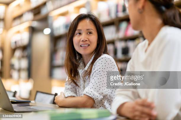 two adult women studying together in the library - annual woman stock pictures, royalty-free photos & images