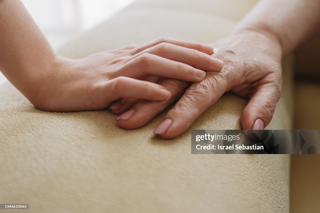Close-up view of an unrecognizable young girl tenderly stroking her grandmother's hand.