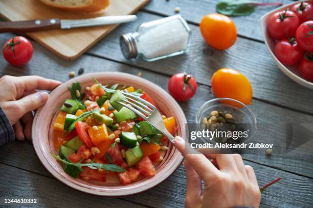 a woman or a girl eats a salad of chopped raw vegetables. chopped tomatoes and cucumbers, with the addition of pine nuts. vegetarian, vegan and raw food food and diet. - rauw voedsel dieet stockfoto's en -beelden