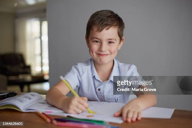young smiling boy child doing homework at the dining room table - sitting at table looking at camera stock pictures, royalty-free photos & images