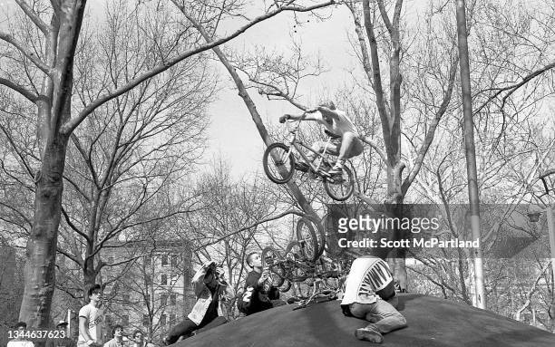 View of a cyclist on a bike as he jumps a row of upturned bicycles in Washington Square Park, in the Greenwich Village neighborhood, New York, New...