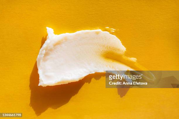 smear of pastel beige body cream on yellow background. concept of natural skin care cosmetic. extreme close-up and flat lay style - aufschäumen stock-fotos und bilder