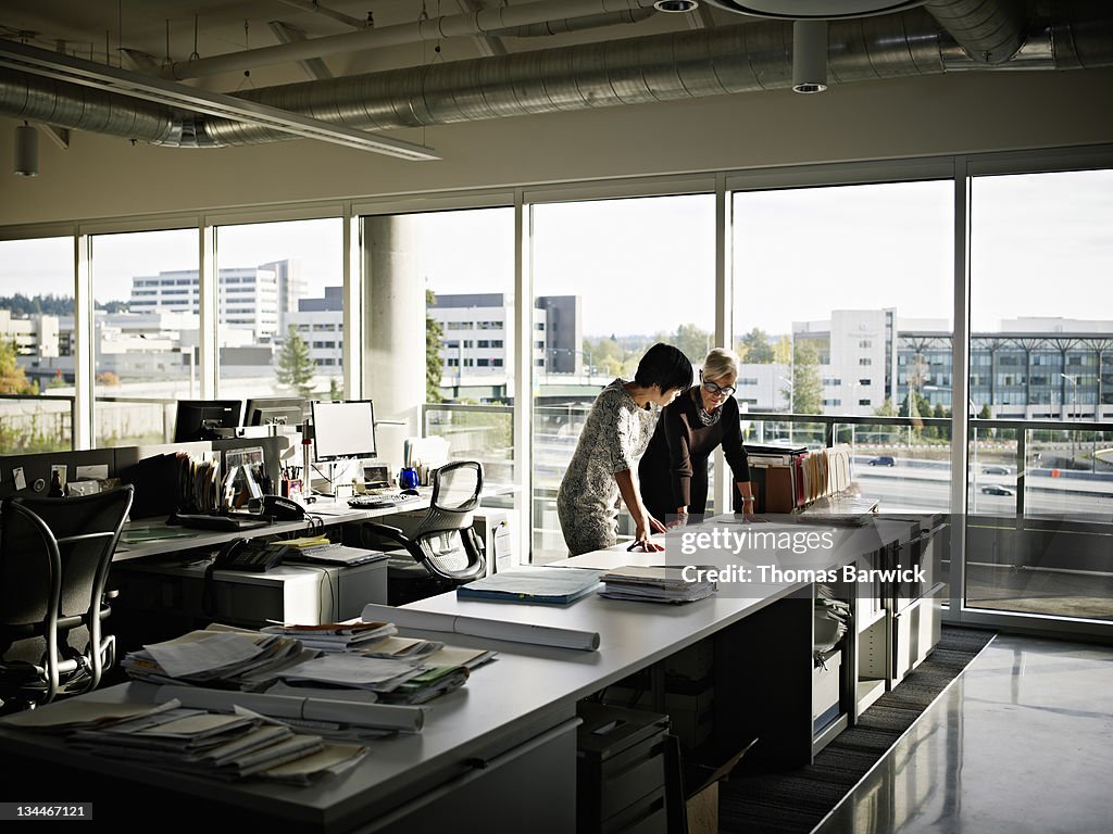 Two female architects examining plans in office
