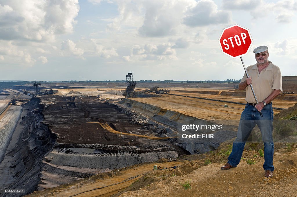 Man standing on the edge of an open pit, holding up a stop sign, Grevenbroich, North Rhine-Westphalia, Germany, Europe