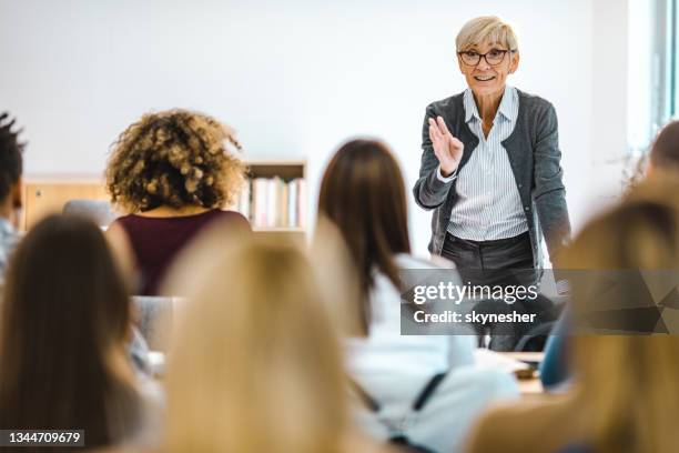 feliz profesora madura dando una conferencia frente a sus estudiantes en la sala de conferencias. - orador fotografías e imágenes de stock