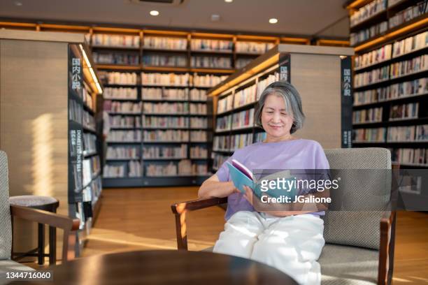 senior woman reading in the library - content japanese ethnicity stock pictures, royalty-free photos & images