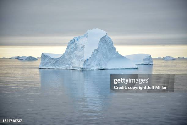 tilted blue iceberg reflected in calm ocean, southern ocean, antarctica. - treibhauseffekt stock-fotos und bilder