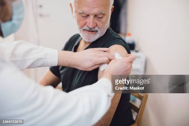 male doctor giving vaccine to senior man in medical clinic during pandemic - schots stock-fotos und bilder
