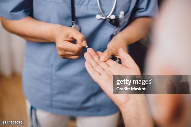 midsection of nurse taking male patient's blood sugar reading in doctor's office - diabète photos et images de collection