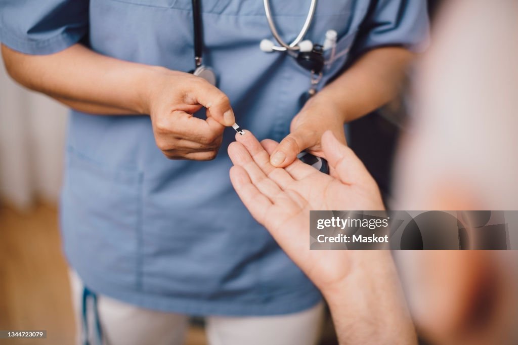 Midsection of nurse taking male patient's blood sugar reading in doctor's office