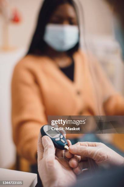 male expertise hands with glaucometer checking female patient's blood sugar at clinic - glaucometer stockfoto's en -beelden