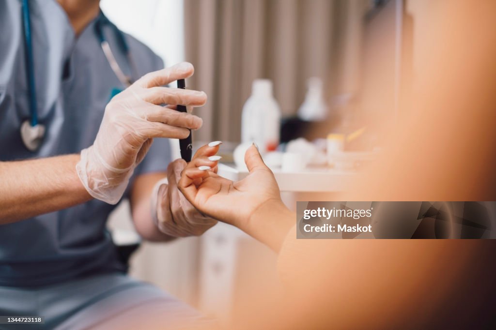 Midsection of male doctor measuring blood sugar through glaucometer in clinic