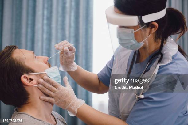 female doctor taking swab test of male patient in clinic during covid-19 - coronavirus stockfoto's en -beelden