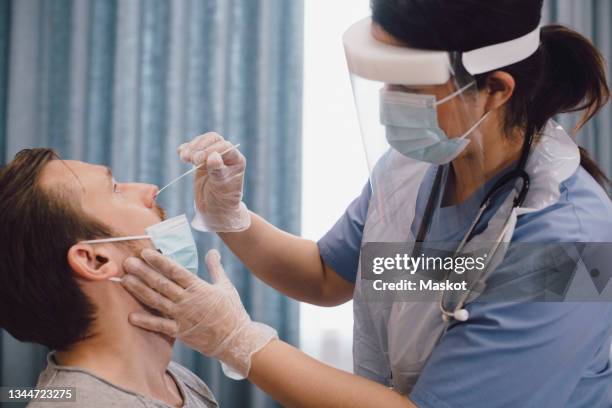 female doctor taking swab test of male patient in clinic during covid-19 - coronavírus - fotografias e filmes do acervo