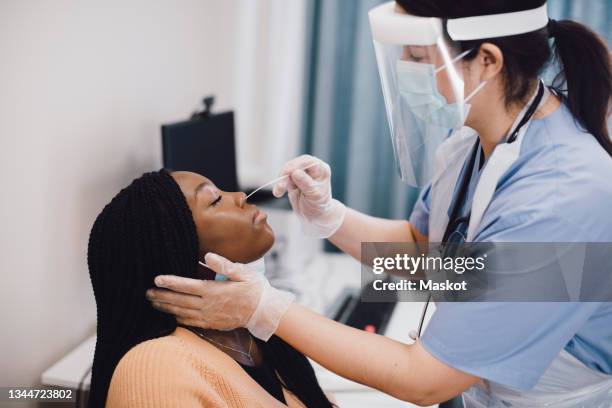 mature nurse taking swab test of female patient at doctor's office during covid-19 - instrumento de la reacción en cadena de la polimerasa fotografías e imágenes de stock