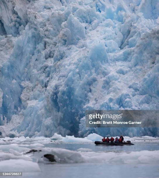 small boat of tourists explore a glacier - glacier calving stock pictures, royalty-free photos & images