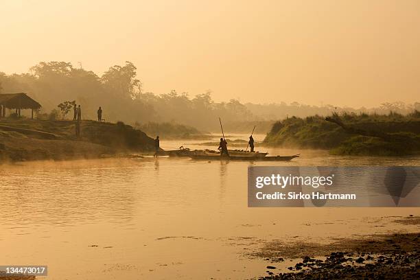 dugout canoe with punting ferryman crossing a small river early in the morning, rising sun and fog, chitwan national park, nepal, asia - chitwan stock pictures, royalty-free photos & images