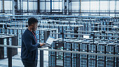 Data Center Engineer Using Laptop Computer. Server Farm Cloud Computing Specialist Facility with African American Male System Administrator Working with Data Protection Network for Cyber Security.