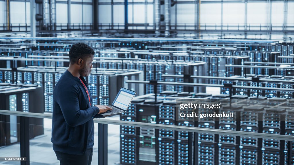 Engenheiro de data center usando laptop. Server Farm Cloud Computing Specialist Facility with African American Male System Administrator Working with Data Protection Network for Cyber Security.