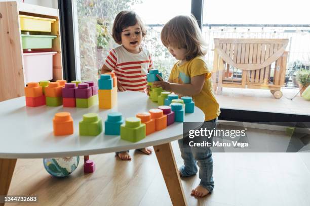 high angle side view of adorable little kids playing with colorful educational toys and blocks at table in modern playroom - pyramid shapes around the house stock-fotos und bilder