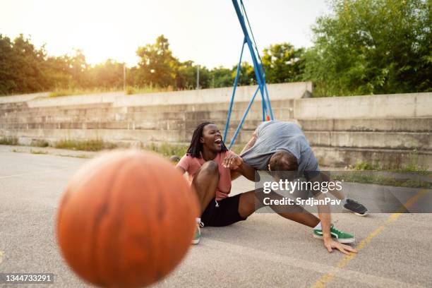 multiracial couple having a laugh after they felt down during pick-up basketball game - foul stock pictures, royalty-free photos & images